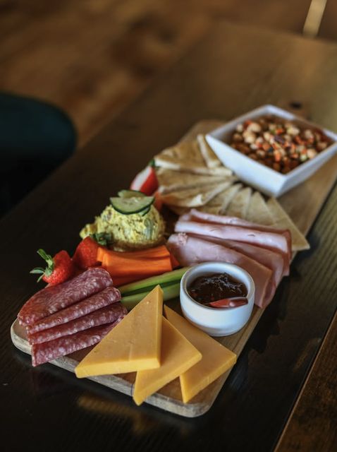 A long charcuterie board with meats, cheeses, vegetables, and pita